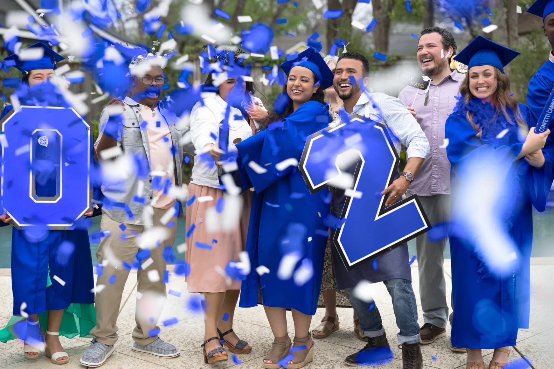 Graduates and family celebrating in a burst of blue confetti