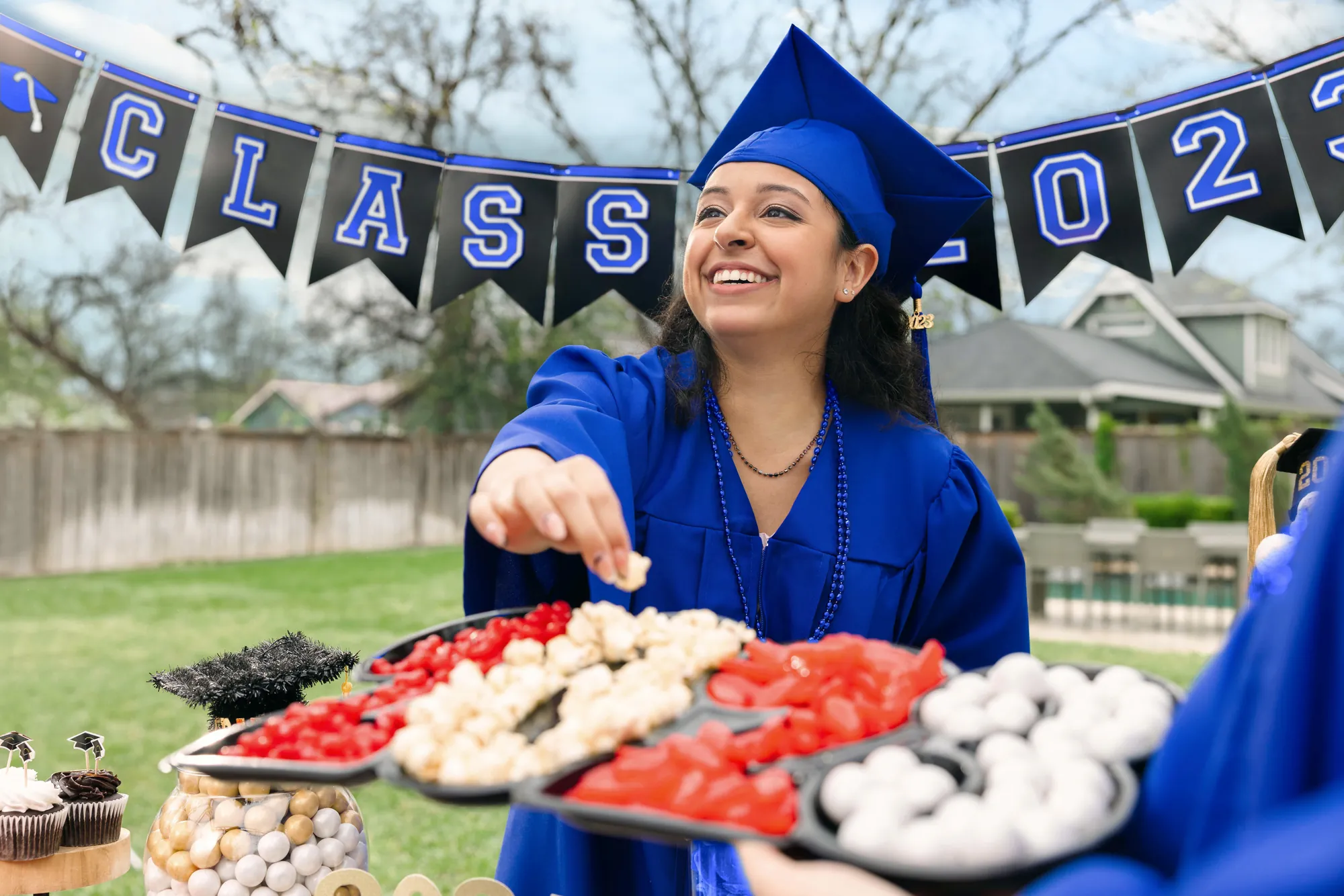 Graduate reaching for a party food spread under a Class of 2023 banner