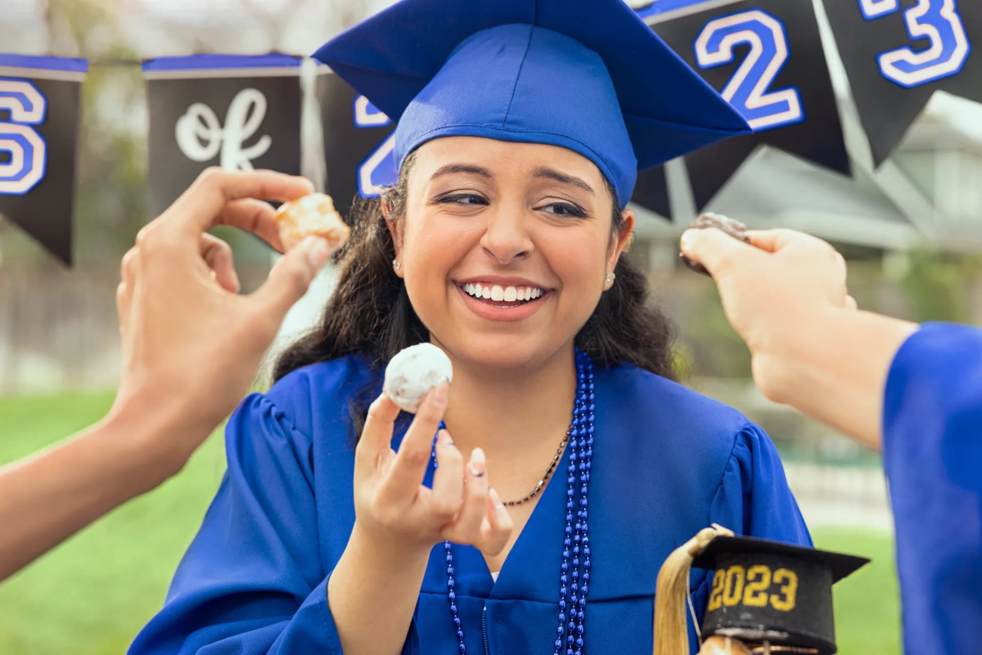 Graduate in a blue cap and gown smiling as friends feed her a treat