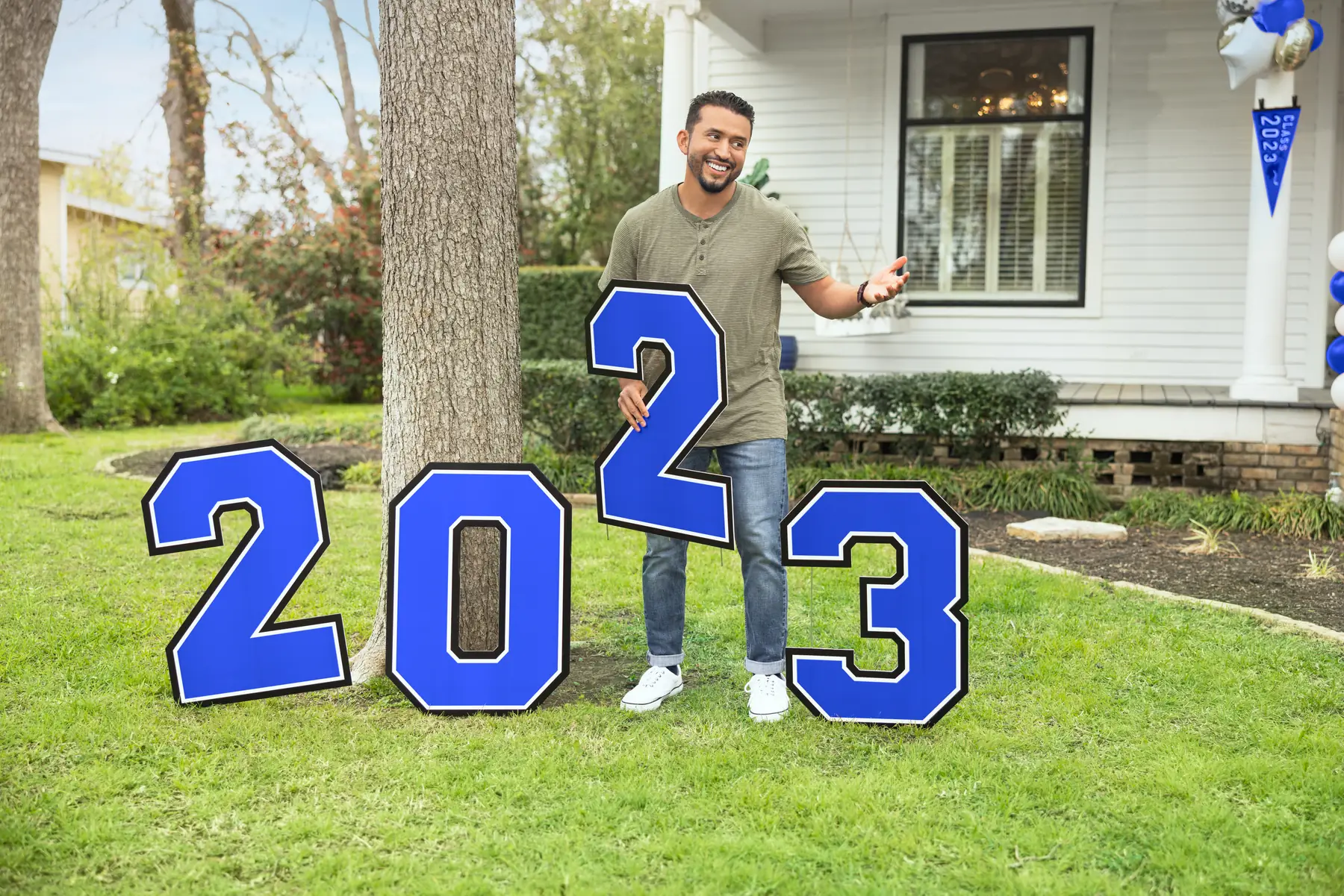 Dad posing beside blue 2023 yard letters on the front lawn