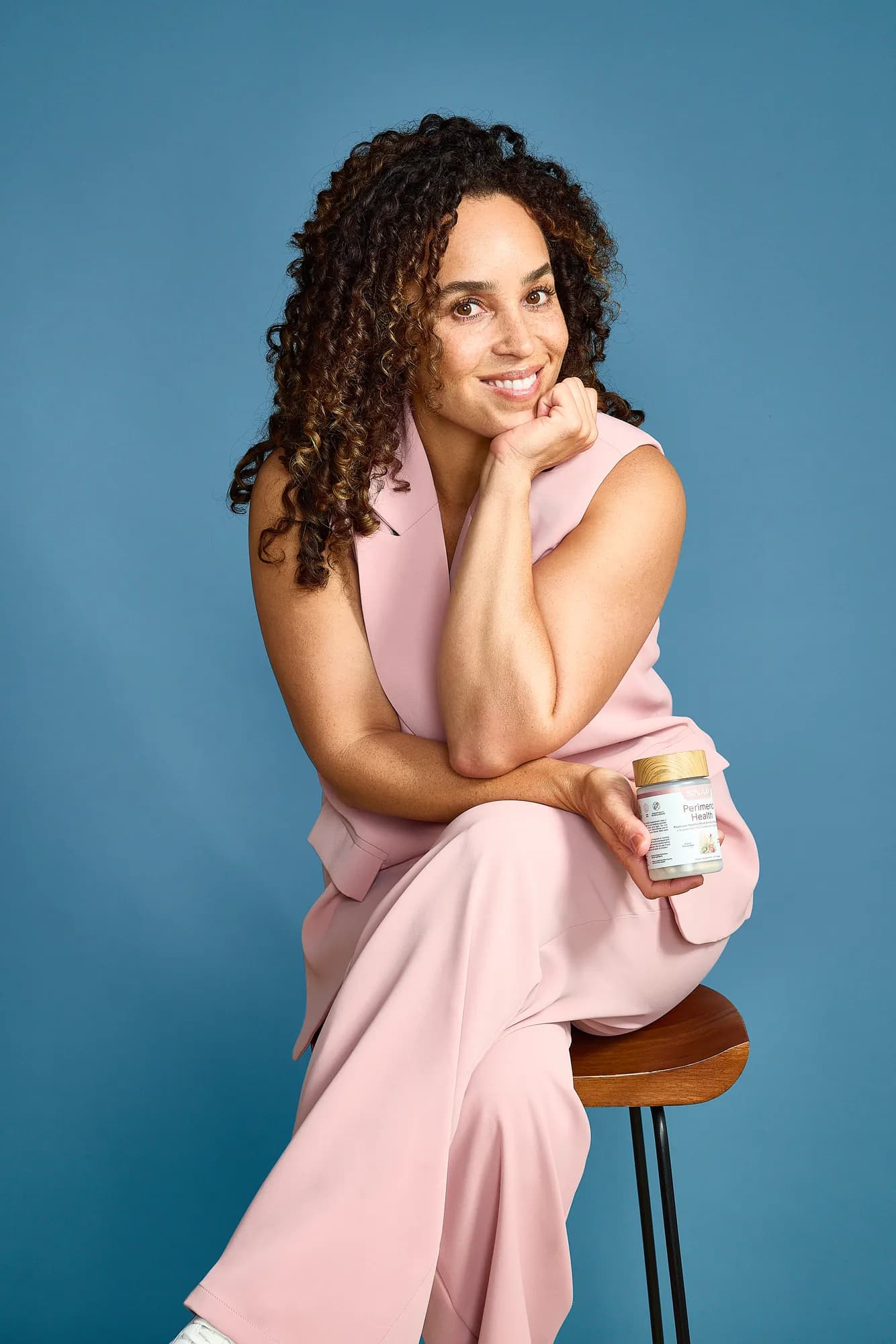 Model seated on a stool with SNAP Supplements on a blue backdrop