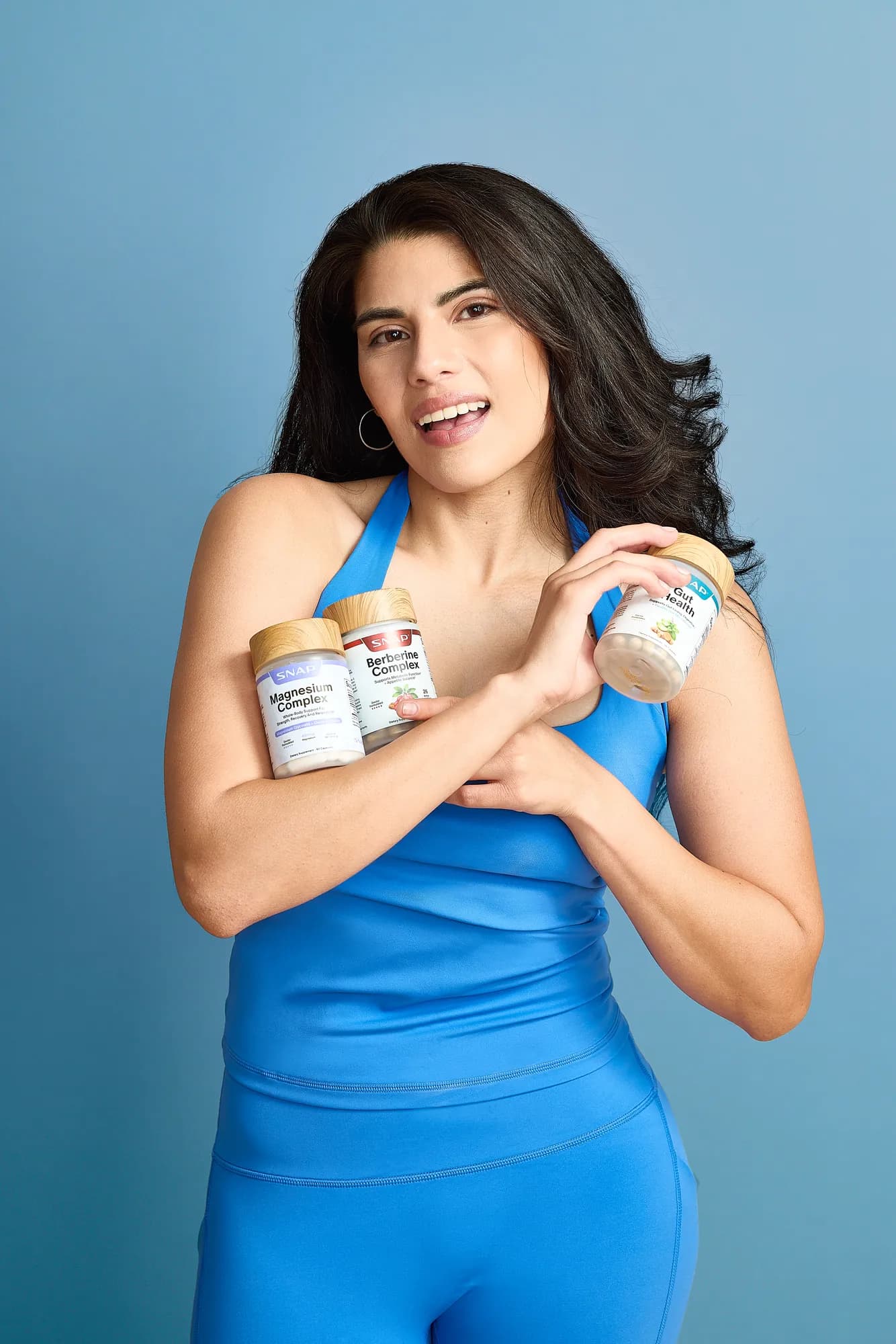Model in blue athleisure holding SNAP Supplements bottles on a blue backdrop
