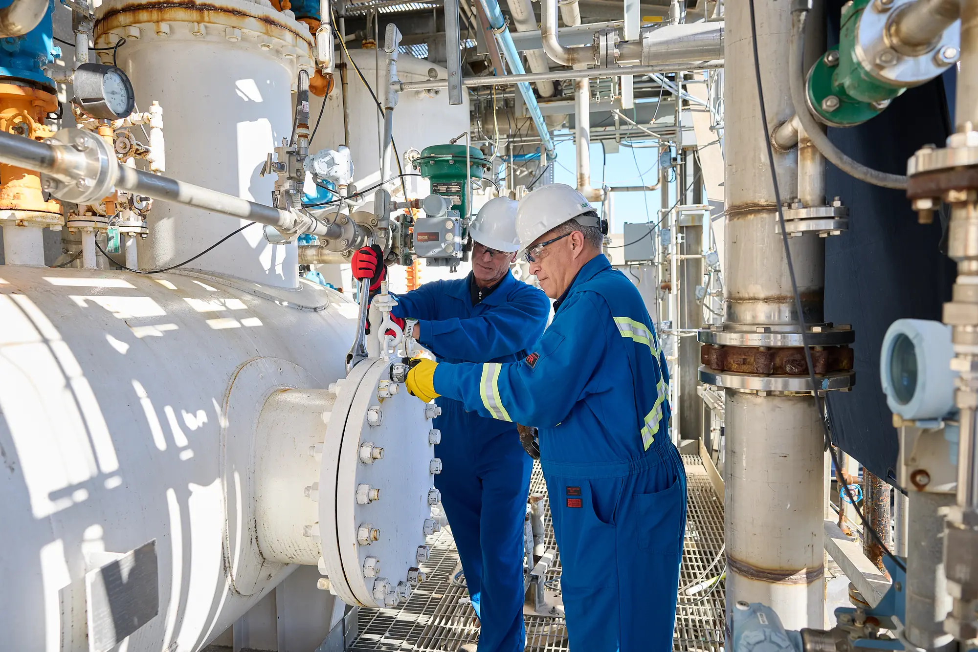 Two workers in coveralls and hard hats inspecting equipment at an industrial plant