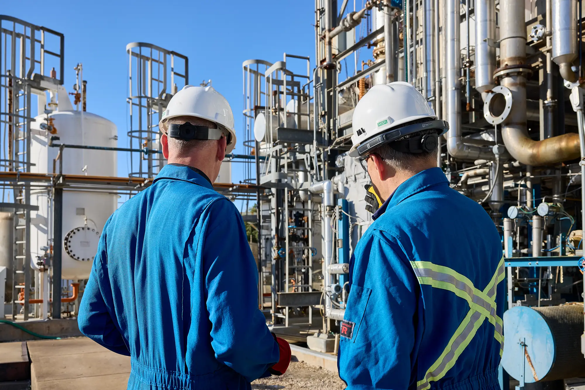 Two workers in coveralls walking through an outdoor plant