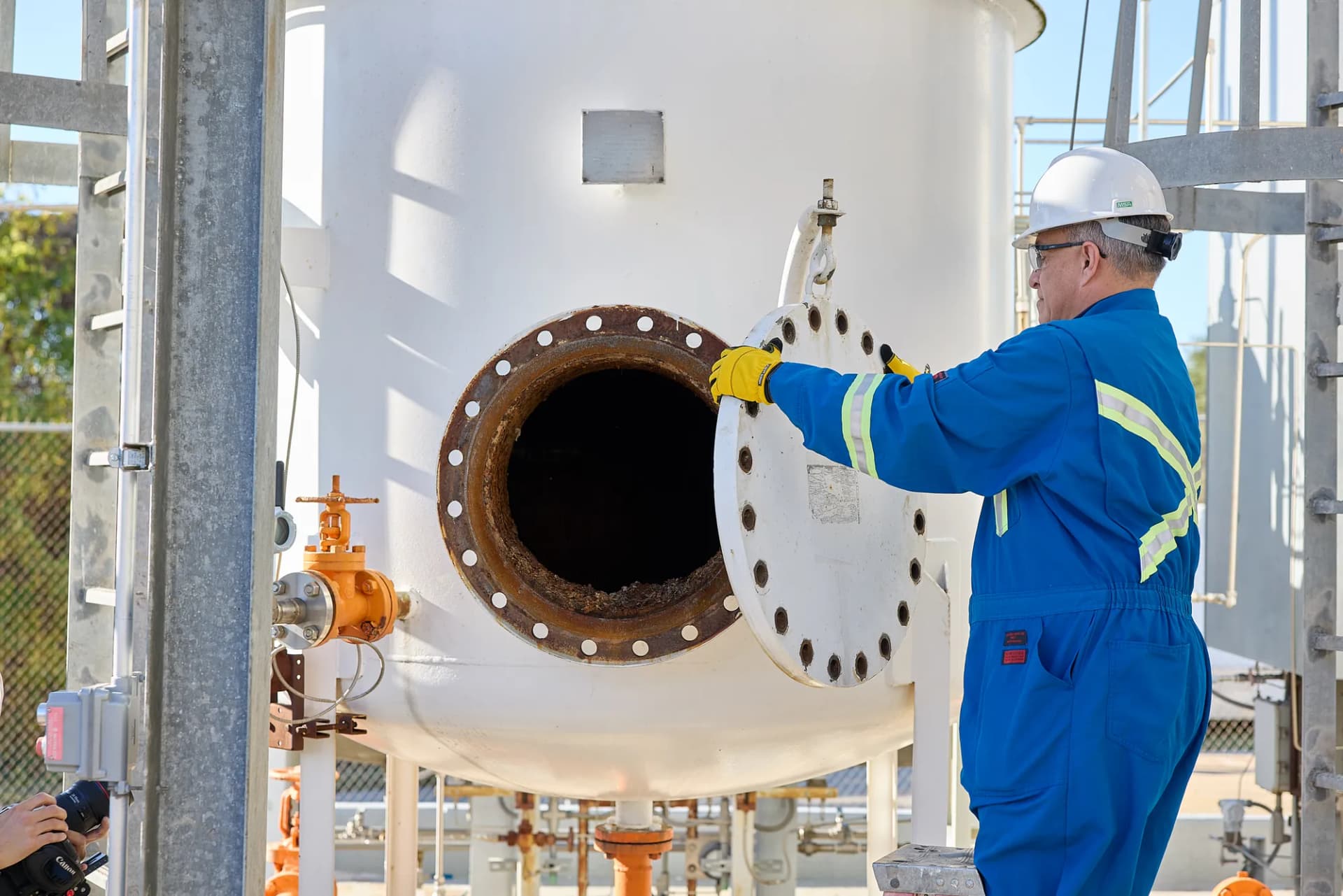 Worker in blue coveralls opening a large white vessel